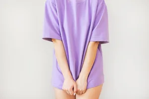 A person is pulling the hem of their purple T-shirt to cover their bare legs A person is pulling the hem of their purple T-shirt to cover their bare legs