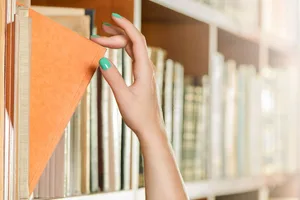 tsundoku A close-up of a hand with green-painted nails selecting a book on a shelf