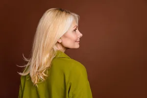 Anti-ageing wardrobe hacks The side profile of a middle-aged woman wearing a green shirt against a brown background.