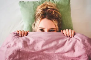 A woman lying in bed with only part of her face visible above the duvet A woman lying in bed with only part of her face visible above the duvet