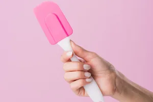 A hand holding a silicone spatula against a pink background A hand holding a silicone spatula against a pink background