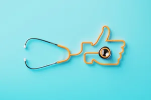 A stethoscope arranged to form the shape of a thumbs up symbol on a blue background A stethoscope arranged to form the shape of a thumbs up symbol on a blue background