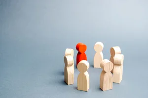 A handful of wooden game pawns, including one red pawn, arranged in a circle on a grey background A handful of wooden game pawns, including one red pawn, arranged in a circle on a grey background