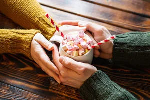 Couple holding hands around a cup of hot chocolate cocoa with heart shaped marshmallow as topping Couple holding hands around a cup of hot chocolate cocoa with heart shaped marshmallow as topping