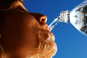 Stay hydrated Woman pours bottle of water into her mouth against a blue background