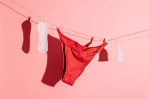 A panty liner, a pair of red underwear and a menstrual cup are hanging on a line against a pink background A panty liner, a pair of red underwear and a menstrual cup are hanging on a line against a pink background
