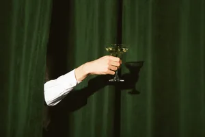 Hand with a martini glass Hand with a martini glass sticks out from the green curtains