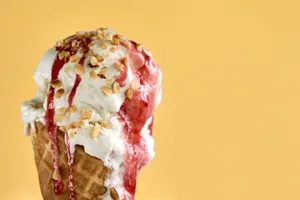 Why ice cream is good for you Vanilla ice cream topped with strawberry sauce and chopped nuts in a cone against a yellow background