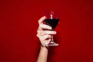 Chilled red wine A hand holds up a glass of red wine in front of a red background