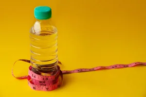 A measuring tape wrapped around a plastic water bottle against a yellow background A measuring tape wrapped around a plastic water bottle against a yellow background