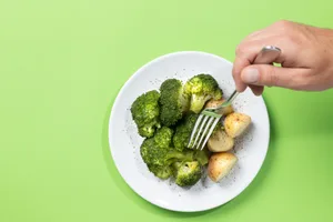 Broccoli shots A hand stabs a fork into a piece of broccoli, which is on a plate against a green background
