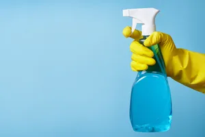 A gloved hand sprays a bottle of cleaning product A gloved hand sprays a bottle of cleaning product