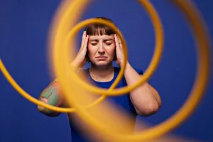 adhd2 Woman with head in hands standing with eyes closed behind spiral cables against blue background