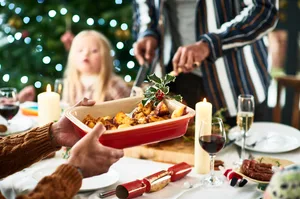 Man holding serving dish with roast potatoes and a sprig of holly for Christmas dinner History of Christmas dinner
