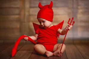 funny baby in devil halloween costume on wooden background funny baby in devil halloween costume with horns and trident on a dark wooden background