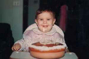 Baby girl’s first birthday Happy baby girl during her first birthday party, with a candle on a homemade cake. 90's celebration. Full shot