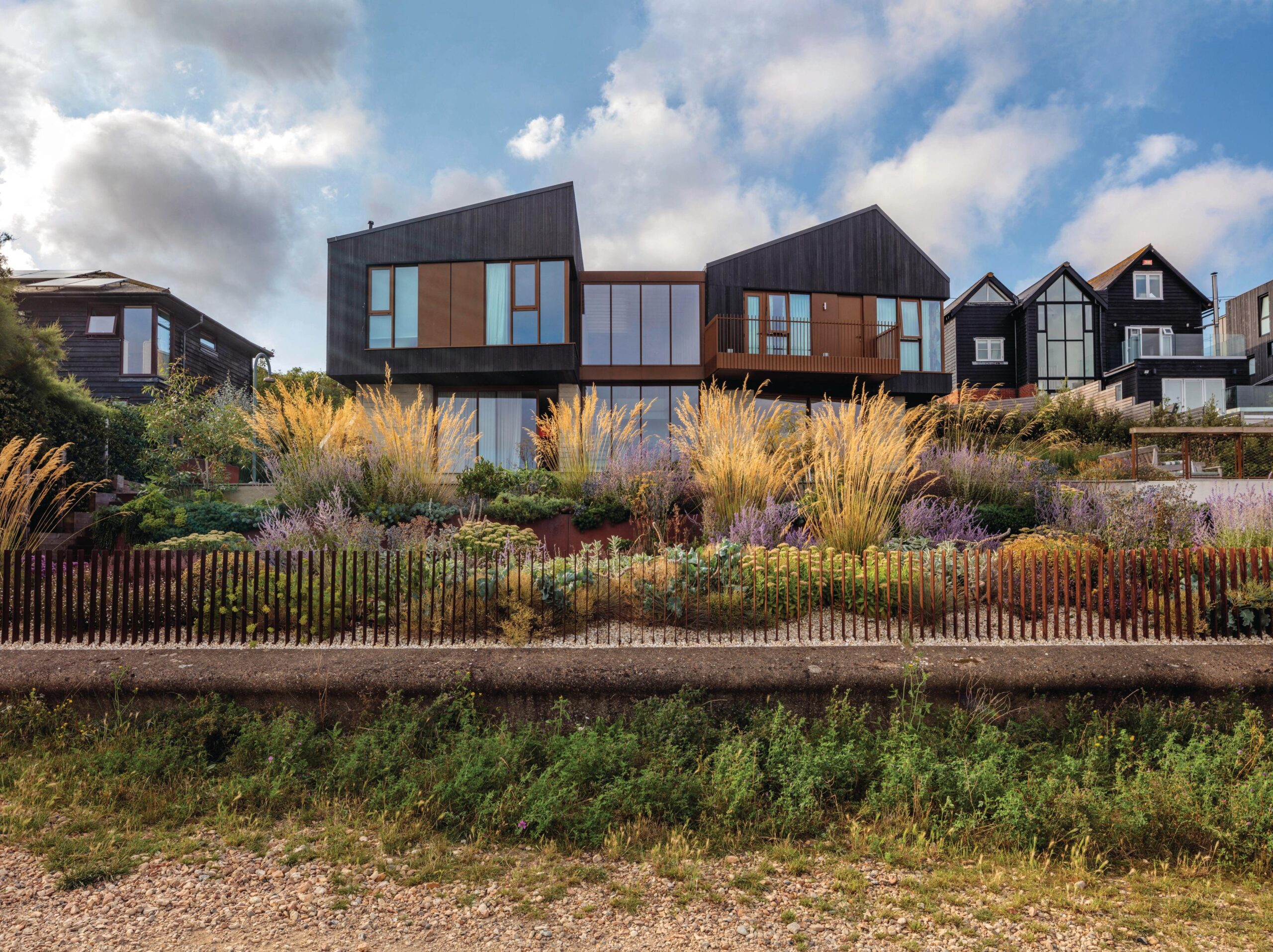 Tall plumes of Stipa gigantea grass form a striking spectacle from the beach, whose grasses, wild alliums and sea kale inspired much of the planting here. House and garden are linked by the use of Corten steel in the detailing.
