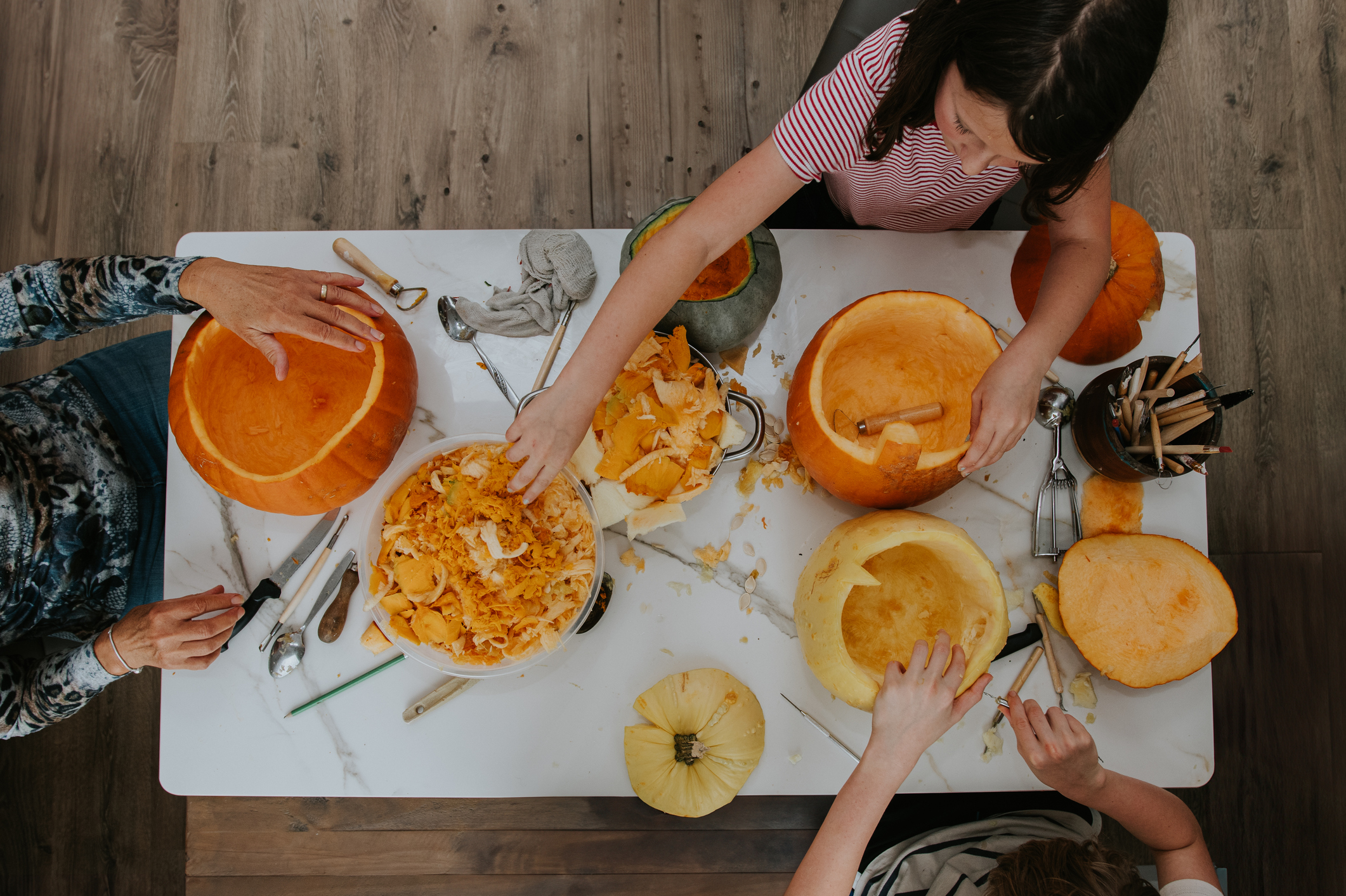 A family make Jack O' Lanterns for Hallowe'en. They sit around a white marble table and concentrate on carving faces into pumpkins. A messy but fun activity. The pumpkins are completely hollowed out. © Getty / Catherine Falls Commercial