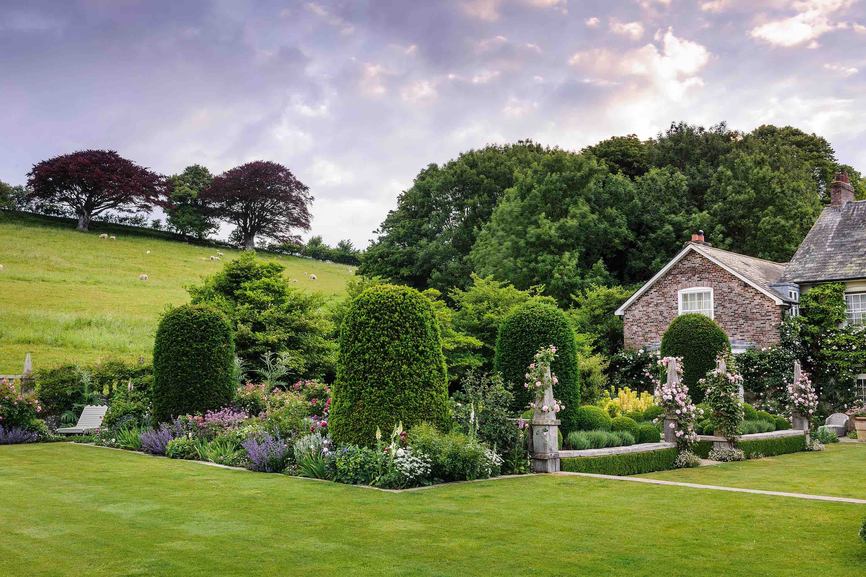 A series of oversized, clipped yews march out from the south-facing terrace and stand guard over the rose garden. Their outline is echoed in the trees beyond, helping to anchor the garden within its setting.