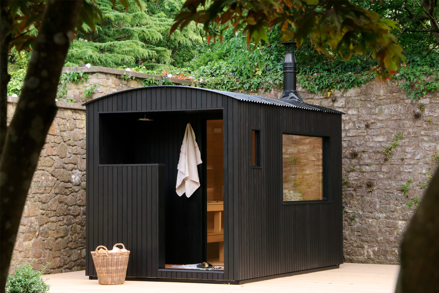 Black sauna hut in the corner of a walled courtyard garden