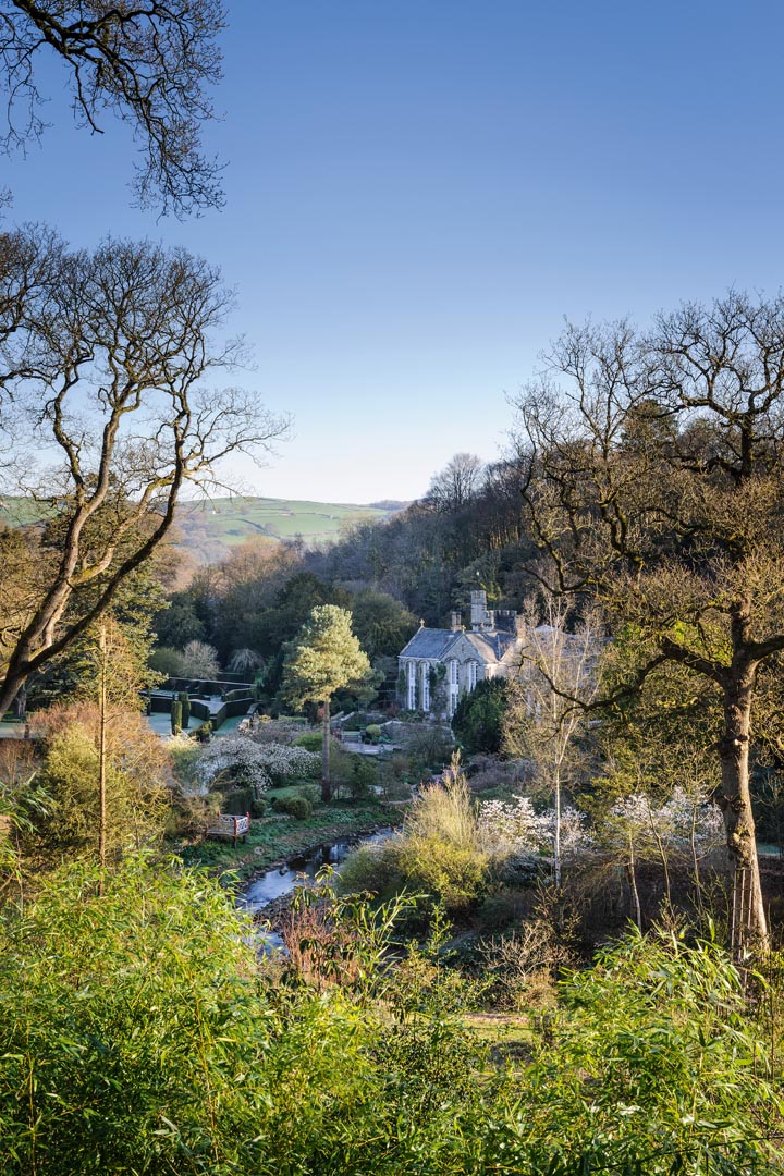 Gresgarth Hall sits at the mouth of a wooded valley, with the brook Artle Beck drawing a sweeping curve as it rushes past the house. Dark yew hedges stamp formality near the house and echo the stone walls etched on the hills beyond.