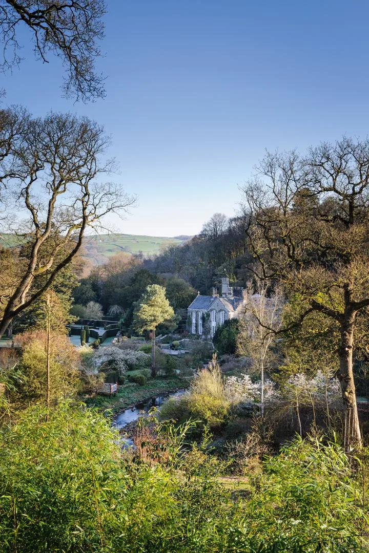 Gresgarth Hall sits at the mouth of a wooded valley, with the brook Artle Beck drawing a sweeping curve as it rushes past the house. Dark yew hedges stamp formality near the house and echo the stone walls etched on the hills beyond.